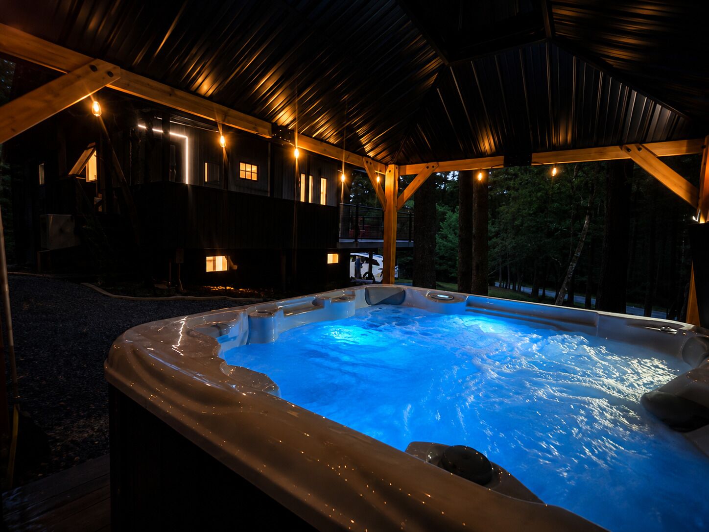 A hot tub with a wooden deck and a covered area with string lights.