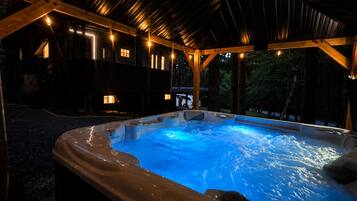 A hot tub with a wooden deck and a covered area with string lights.