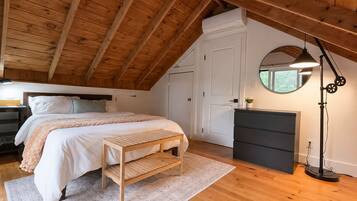 A bedroom with a sloped ceiling, a bed with a bench, a dresser, a mirror, and a floor lamp.