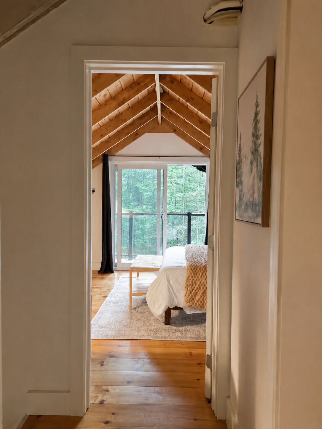 A bedroom with a large window, a bed, and a wooden floor.