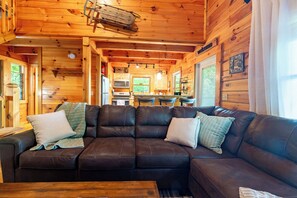 A wooden cabin interior with a leather sofa, wooden walls, and a kitchen area. - private smoky mountain retreat. Views + Arcade (Sevierville)