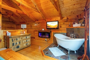 A wooden cabin interior with a fireplace, a television mounted on the wall, a wooden cabinet, and a freestanding bathtub. - private smoky mountain retreat. Views + Arcade (Sevierville)