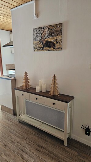 Ein Holzkonsolentisch mit einer weißen Schubladenkommode, einer kleinen Ablage mit Kerzen und einer Tannenzweigdruck, sowie ein Bild eines Elchs an der Wand.