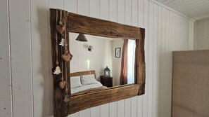 Ein rustikaler Spiegel mit Holzrahmen, der ein Bett und einen Nachttisch darin zeigt.