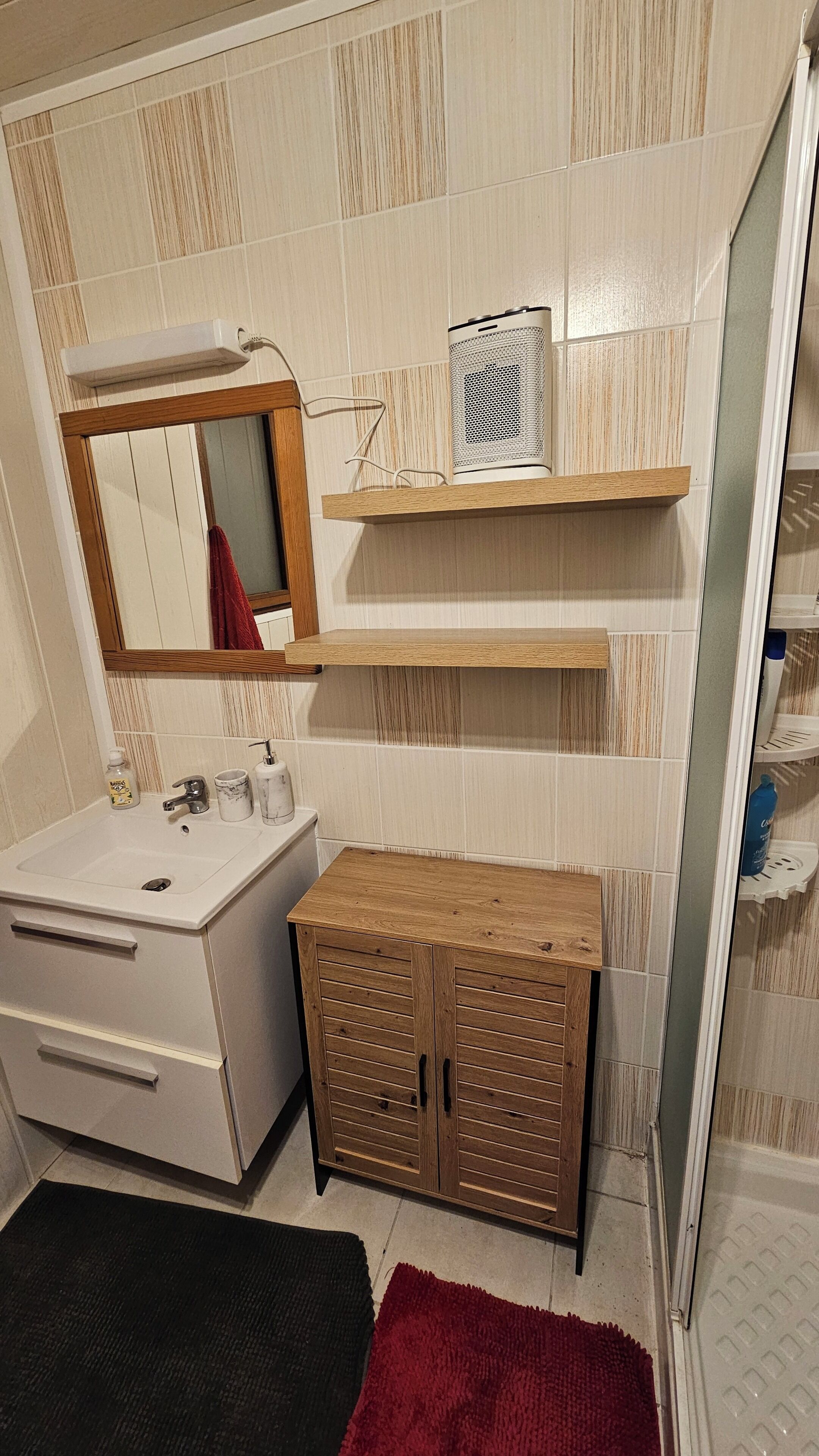 Un baño con lavamanos blanco, un espejo, un armario de madera y zona de ducha.