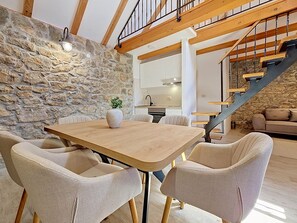 A dining area with a wooden table and wicker chairs, a stone wall, a kitchen in the background, and a staircase. - Vacation home Ana by Interhome (Trilj)