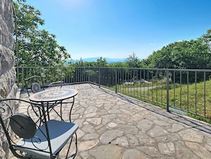 A stone patio with a round table and chairs, a metal railing, and a view of greenery and distant mountains. - Vacation home Marija by Interhome (Trilj)