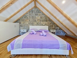 A bedroom with a stone wall, wooden beams, a bed with purple bedding, and a white wardrobe. - Vacation home Marija by Interhome (Trilj)