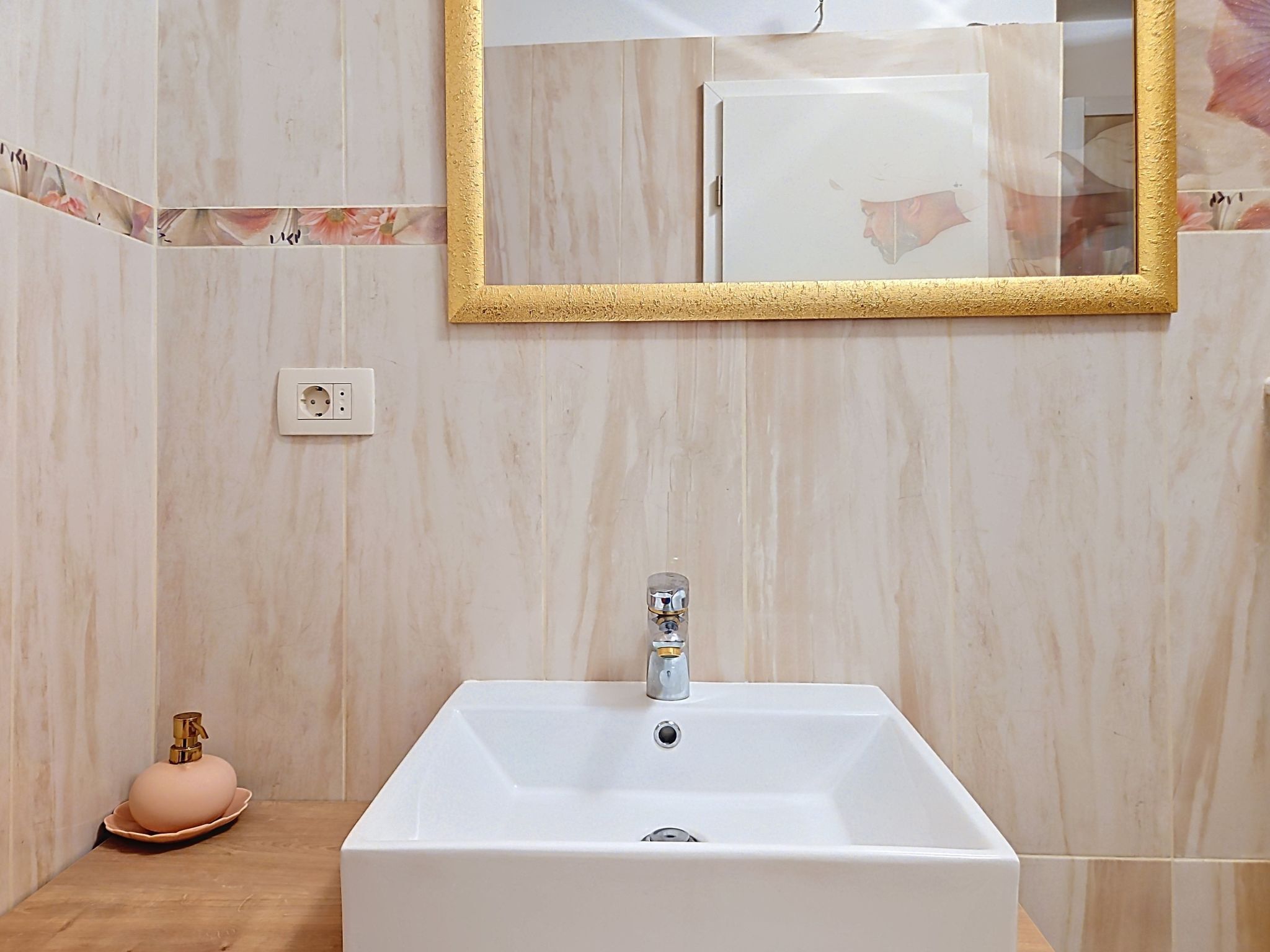 Un baño con un lavamanos blanco, un espejo con marco dorado y un jabonera rosa.