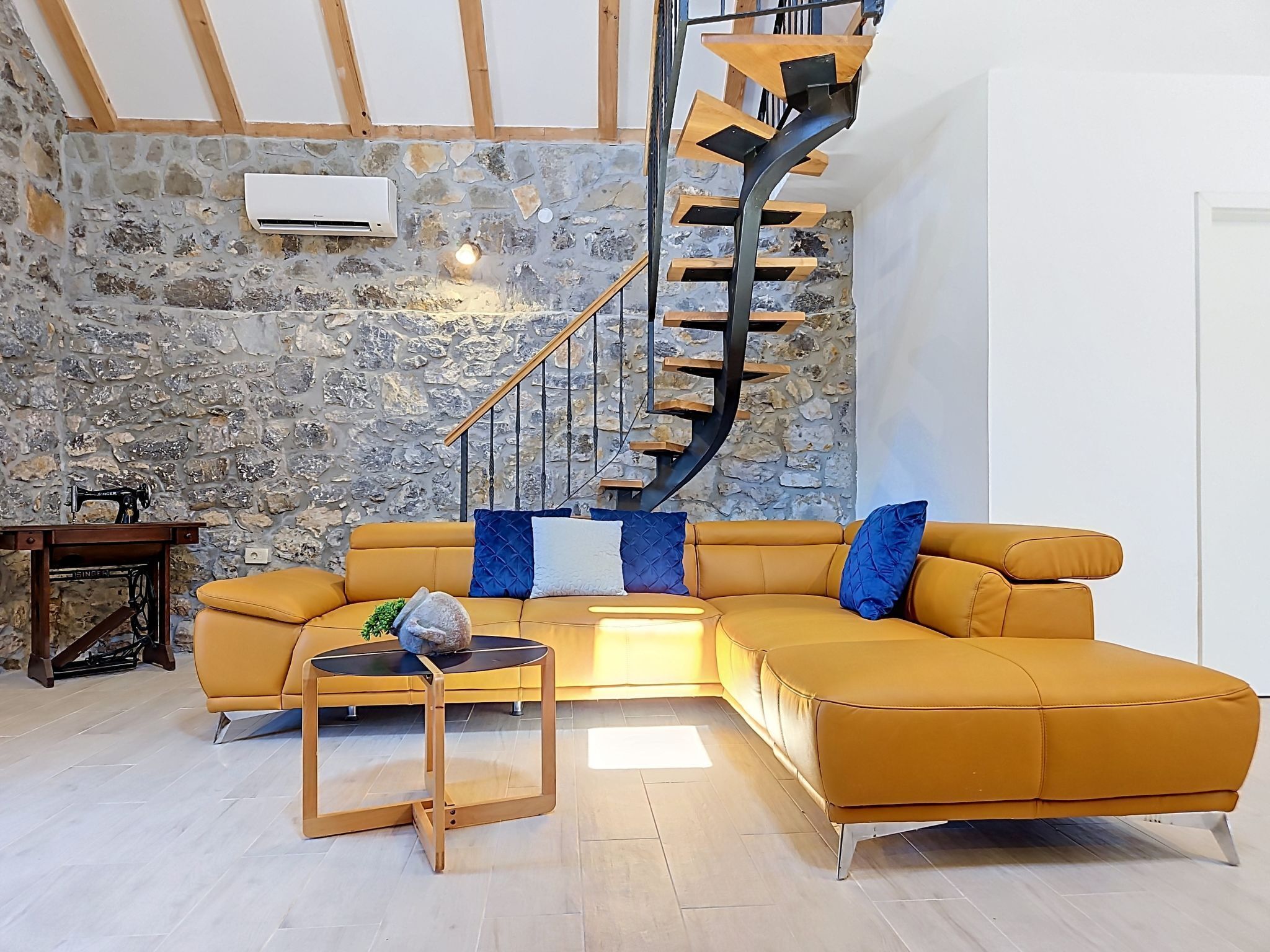A modern living room with a curved staircase, stone wall, and a sectional sofa.