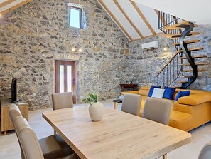 A spacious room with a stone wall, a wooden dining table, a sofa, and a spiral staircase. - Vacation home Marija by Interhome (Trilj)