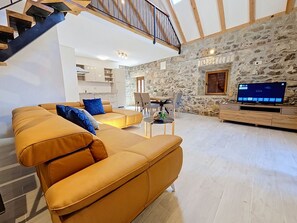 A modern living room with a sectional sofa, a dining table, and a stone wall. - Vacation home Marija by Interhome (Trilj)