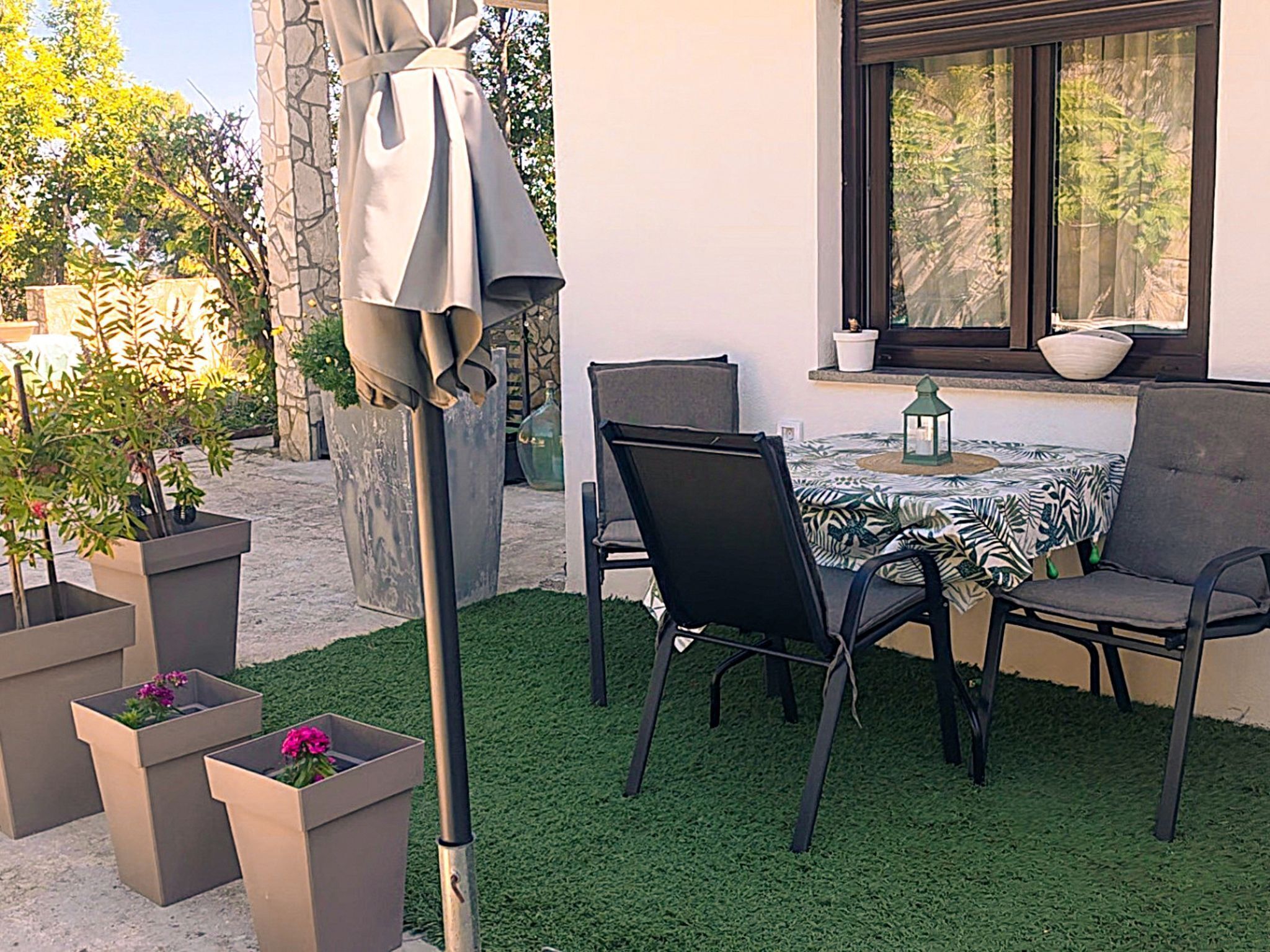An outdoor patio with a table and chairs, surrounded by planters and a stone wall.