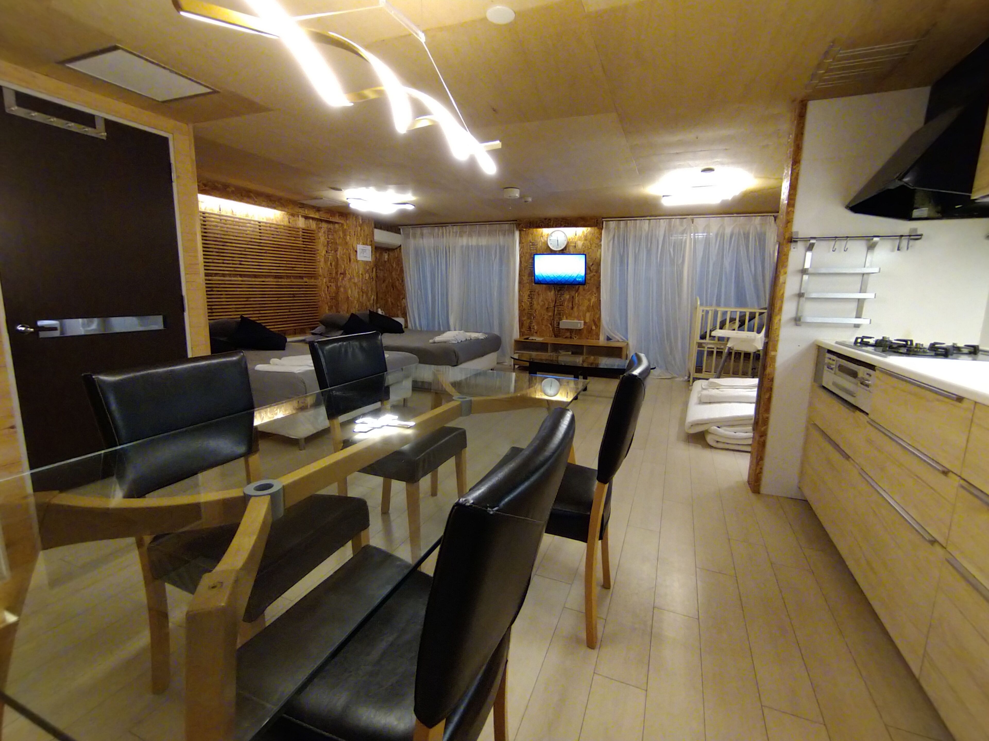 A modern kitchen with a dining area, wooden flooring, and a TV mounted on the wall.