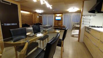 A modern kitchen with a dining area, wooden flooring, and a TV mounted on the wall.