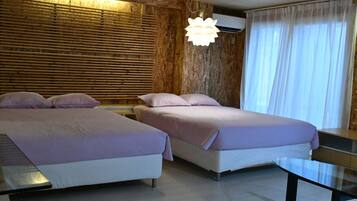 A hotel room with two beds, a wooden wall, an air conditioning unit, a glass table, and a large window with curtains.
