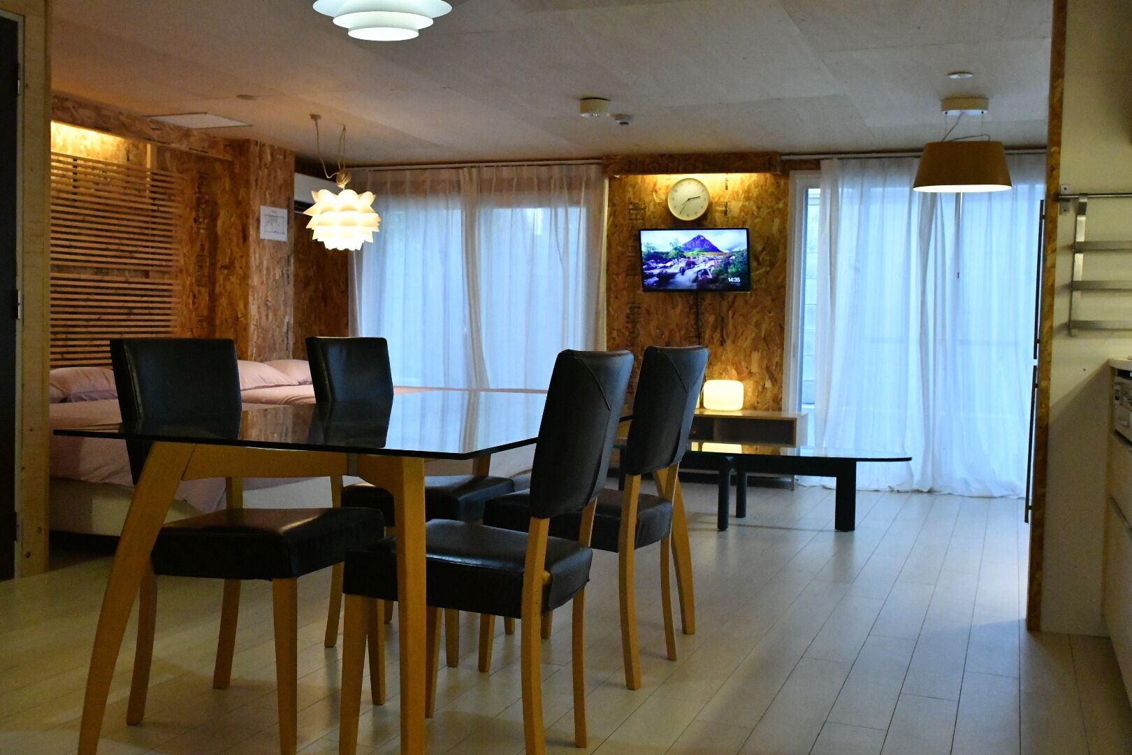 A modern living room with a dining area, wooden accents, a flat-screen TV, and a sofa.