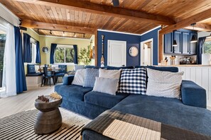 A cozy living room with a blue sofa, wooden ceiling beams, and a view to the kitchen. - Clear Lake Getaway Boat Parking + Lake Access (Clearlake Oaks)
