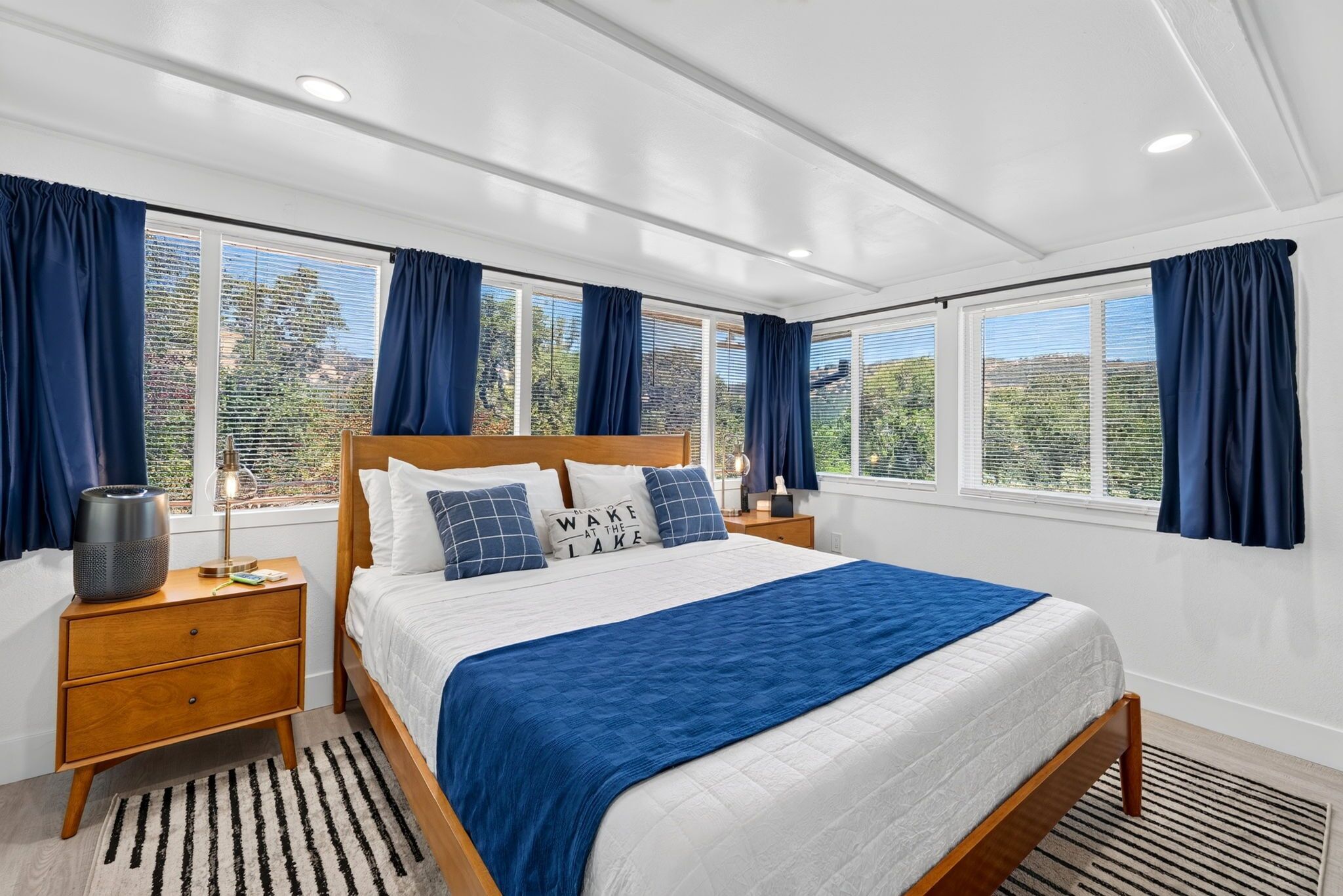 Een slaapkamer met een groot bed, een nachtkastje met een lamp en een raam met gordijnen.