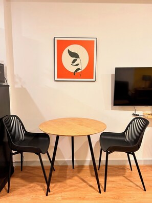 A room with a round wooden table, two black chairs, a framed artwork on the wall, and a television on the right. - Soho residence studio apartment (Ho Chi Minh City)