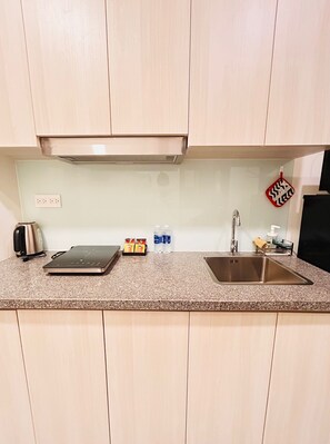 A kitchen with light wood cabinets, a granite countertop, a stainless steel sink, a toaster, a kettle, and a box of tea bags. - Soho residence studio apartment (Ho Chi Minh City)