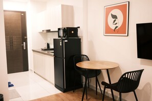 A compact kitchen with a refrigerator, a microwave, and a kettle. There is a small dining table with two chairs. - Soho residence studio apartment (Ho Chi Minh City)