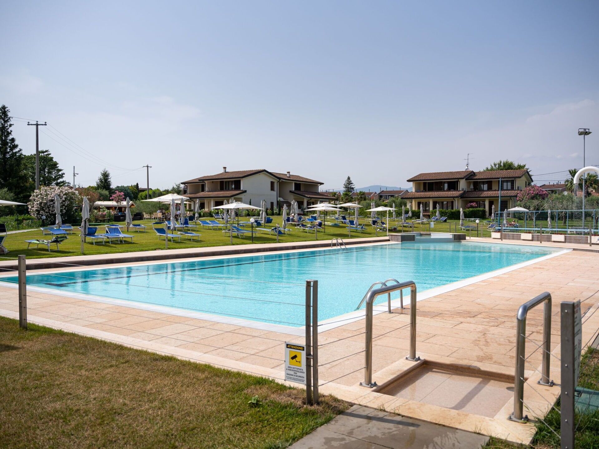 A swimming pool with sun loungers and umbrellas, surrounded by buildings with a view of the landscape.