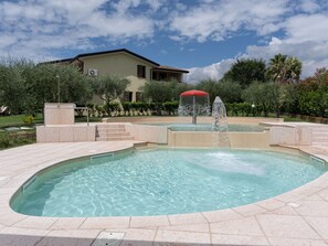 Ein Pool mit Springbrunnen, umgeben von einem angelegten Garten, und ein Haus im Hintergrund.