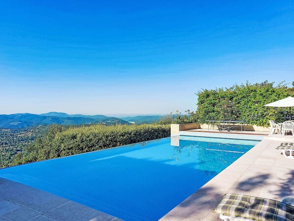 Une piscine avec vue sur les montagnes lointaines, une terrasse avec des chaises et une table.