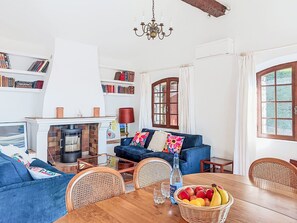 A cozy living room with a fireplace, a blue sofa, a dining table with chairs, and a bookshelf filled with books. - Balcon d´Azur by Interhome (Spéracèdes)