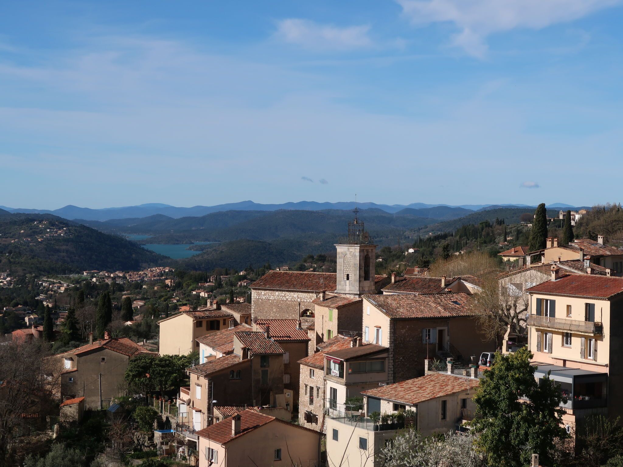 A town with traditional architecture, a prominent tower, and a view of distant mountains.