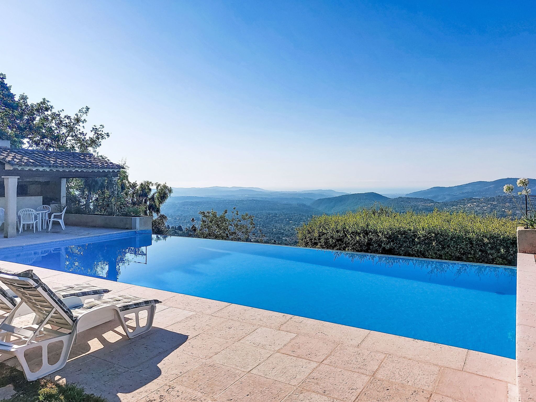 Une magnifique piscine à débordement d’un bleu profond, dotée de chaises longues et offrant une vue sur les montagnes lointaines.