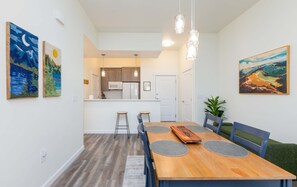 A dining area with a wooden table, chairs, and a kitchen in the background. - Downtown Nampa Condo Close to Idaho Center & NNU (Nampa)
