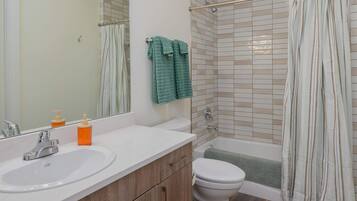 A bathroom with a sink, mirror, toilet, and shower.