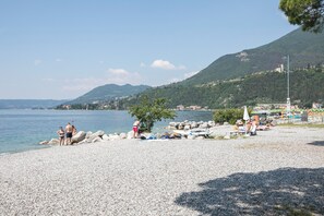 Ein Kiesstrand mit Personen, einem Boot und einem Berg im Hintergrund.