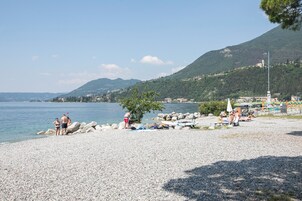 A pebbled beach with people, a boat, and a mountain in the background.