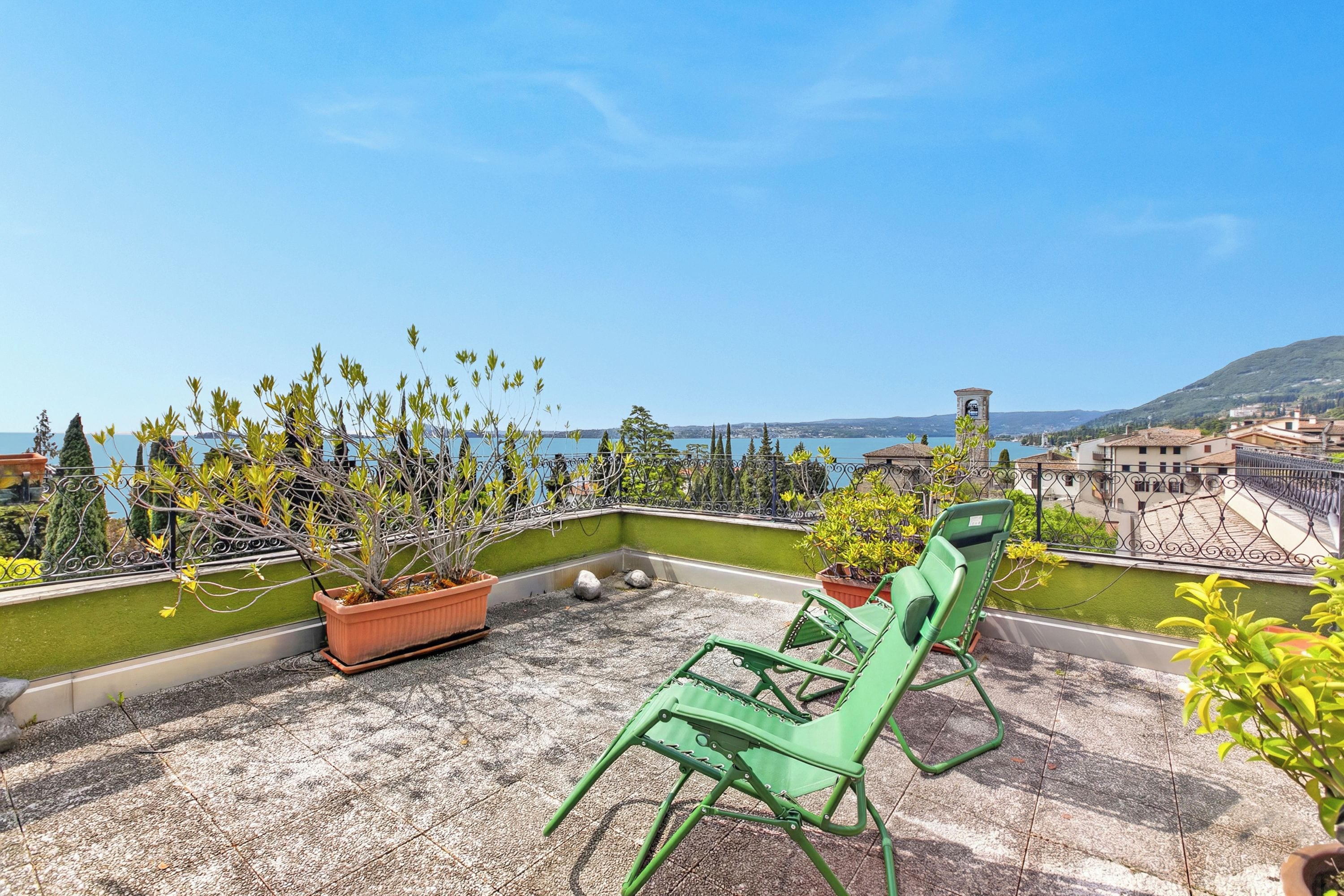 Eine Dachterrasse mit Blick auf das Meer, mit Kübelpflanzen und grünen Stühlen.