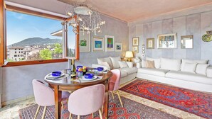 A modern living room with a white sofa, a dining table with pink chairs, and a chandelier. - Roma 62 Lake View,terrace & Private Park (Toscolano Maderno)
