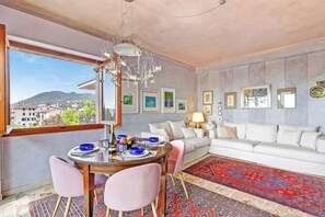 Ein modernes Wohnzimmer mit einem weißen Sofa, einem Esstisch mit rosafarbenen Stühlen und einer Kristallleuchtre.
