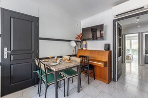 A dining area with a wooden table, chairs, and a television mounted on the wall. - Design 2BR | Private Parking, Beach & Train (Golfe Juan Vallauris)