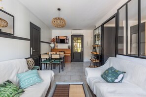 A modern living room with a sofa, a dining area with a table and chairs, and a kitchen in the background. - Design 2BR | Private Parking, Beach & Train (Golfe Juan Vallauris)