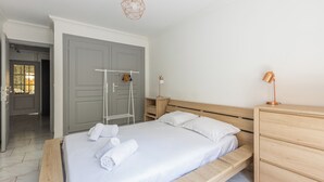 Un dormitorio con cama, cómoda de madera, mesita de noche, lámpara colgante y una puerta con toallero.