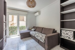 Un saló modern amb un sofà modular, una làmpada penjant decorativa i vista a un balcó amb verdura.
