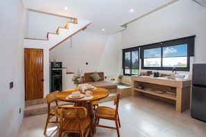 A modern kitchen with a dining area, wooden furniture, and a view through large windows.