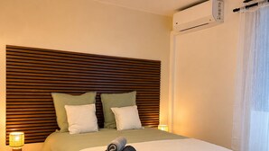 Una cama bien hecha con cabecera, una lámpara de noche y una toalla enrollada sobre la cama.