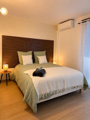 A neatly made bed with a headboard, a bedside lamp, and a rolled towel on the bed. - Urban Beach Apartment. (Saint-Pierre)