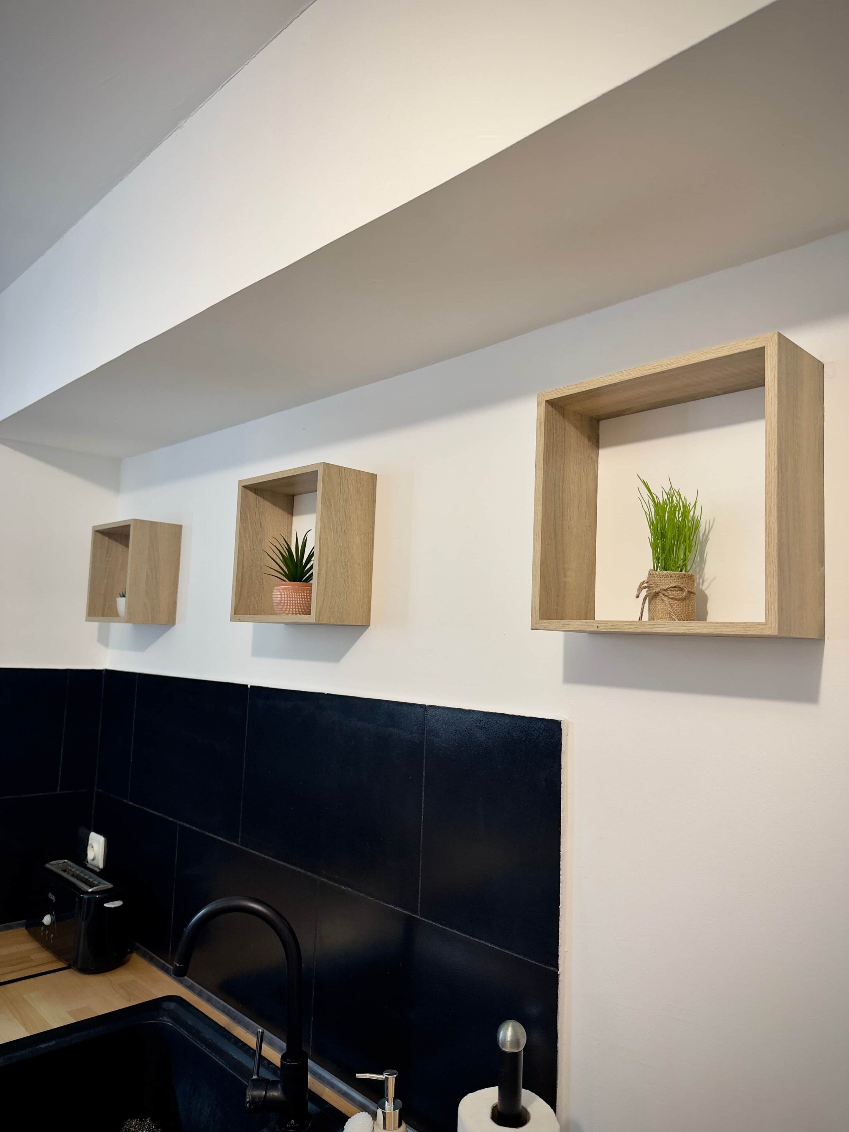 A modern kitchen with black tiles, a sink, and wooden shelves with plants.