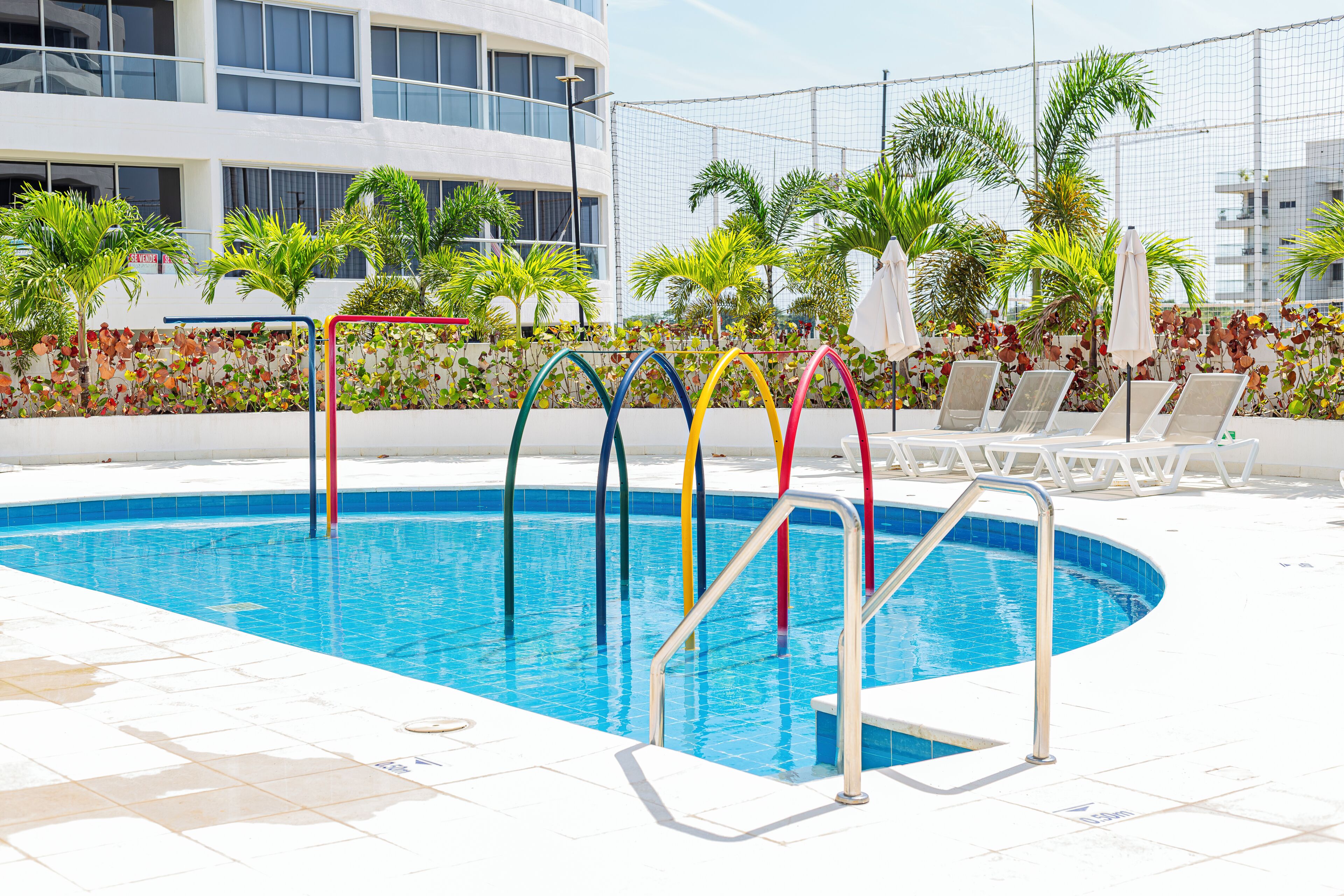 Piscina con escalones coloridos, sillas de descanso y palmeras.