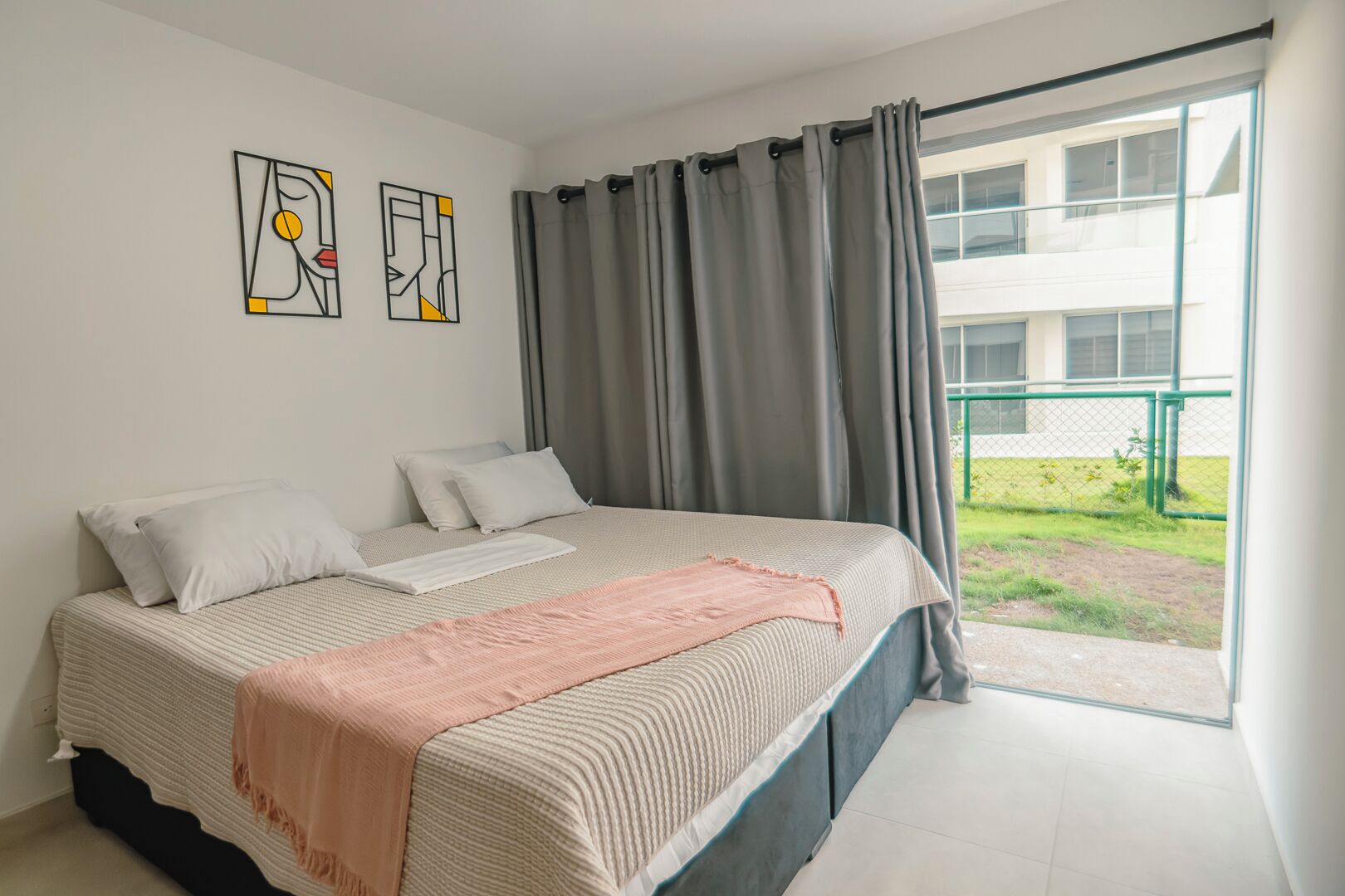Een slaapkamer met een bed, twee kussens, een deken en een raam met gordijnen.