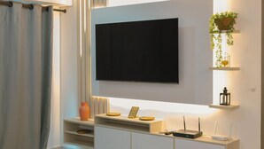 A modern living room with a flat-screen TV mounted on the wall, a white console table with decorative items, and a small plant hanging from the ceiling. - Apto moderno en Serena con balcon  (Cartagena)